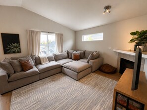 A living room with a sectional sofa, a fireplace, and a large window.