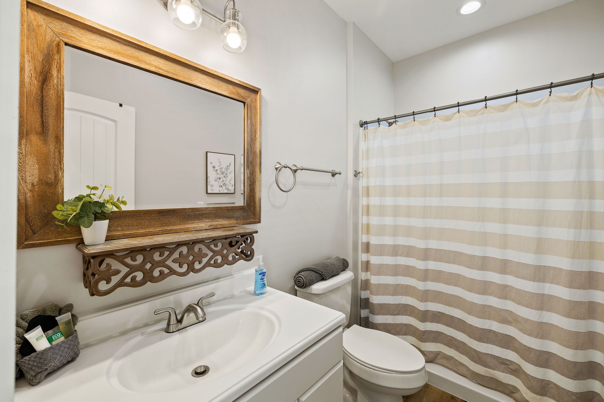 A bathroom with a wooden-framed mirror, a white sink, a toilet, and a striped shower curtain.