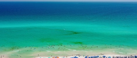 A beach with clear turquoise water, white sand, and numerous umbrellas.