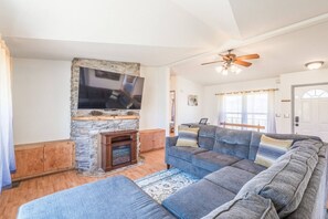 A living room with a stone fireplace, a large sofa, and a ceiling fan.