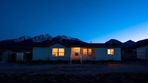 Une maison de plain-pied avec un porche à l’avant, un petit garage attenant et une vue sur les montagnes en arrière-plan.