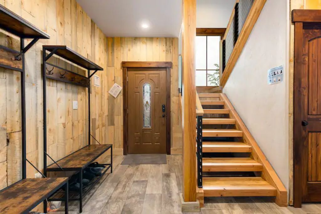 A wooden interior with a staircase, a bench, and a door with a glass panel.