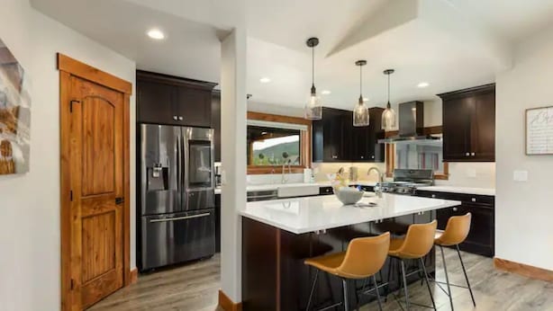 Una cocina moderna con una isla central, taburetes de bar y electrodomésticos de acero inoxidable.
