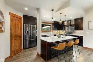 A modern kitchen with a central island, bar stools, and stainless steel appliances. - NEW! Single family home w/ Rooftop Deck & Salt Water Hot Tub (Frisco)