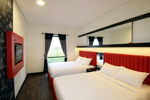 Habitación de hotel con dos camas, televisión, ventana con cortinas y una pared de acento roja.