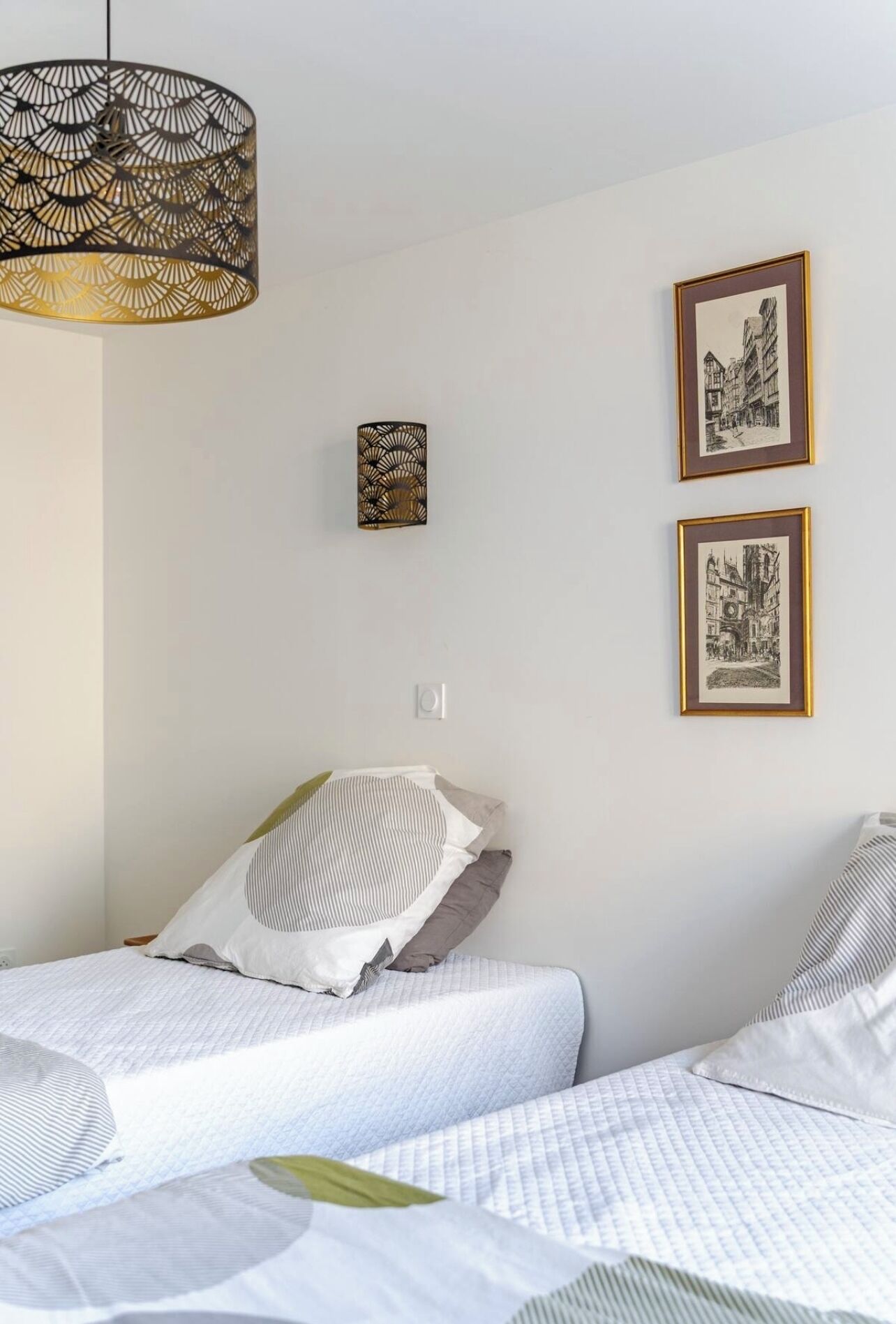 Ein Schlafzimmer mit einem Bett, einer Hängelampe und zwei gerahmten Bildern an der Wand.