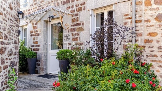 Un bâtiment en pierre doté d’une terrasse en bois, d’une porte et de plantes en pot.