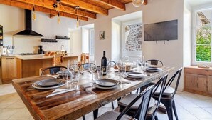 Un coin repas avec une table en bois dressée pour six personnes, une cuisine en arrière-plan et un mur en pierre sur lequel est fixée une télévision.