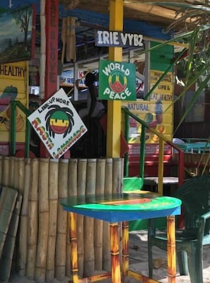 A colorful outdoor seating area with a table and chairs, surrounded by bamboo structures and various signs promoting health and peace.