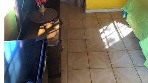 Una stanza piccola con pareti gialle, una tenda marrone, un letto verde e un tavolo con un vaso di fiori.