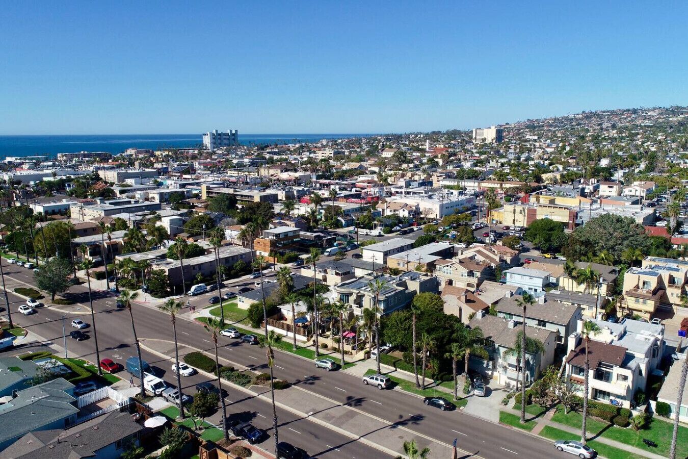 An aerial view of a residential area with streets, houses, and a distant view of the ocean.