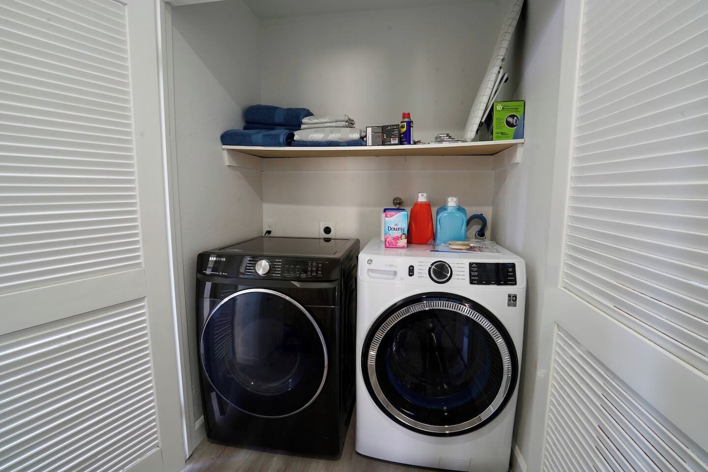 A laundry room with two washing machines, a shelf with folded clothes, and laundry supplies.