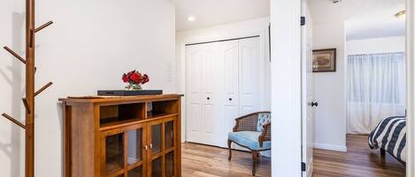 A room with a wooden cabinet, a chair, a bed, and a white door.