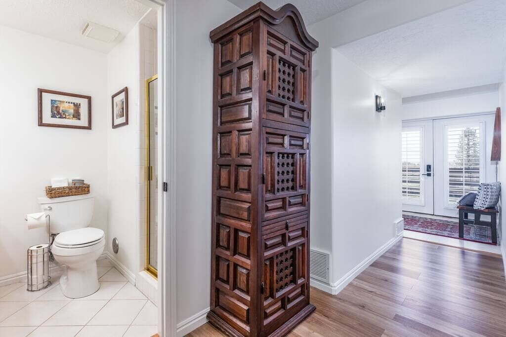 Un couloir avec une armoire en bois, des toilettes blanches et une porte donnant sur un balcon.