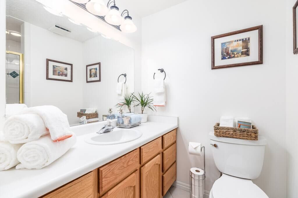 Un baño moderno con tocador blanco, armarios de madera, un espejo grande y un inodoro con una cesta de toallas.