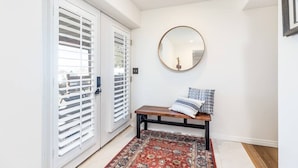 Un couloir avec un banc, un miroir rond et un tapis à motifs.