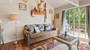A cozy living room with a brown leather sofa, a coffee table, and a large window with curtains. - 2 bed 2 bath Rustic roost loft condo; deck 2 pools; Lake Taneycomo, & amenities  (Branson)