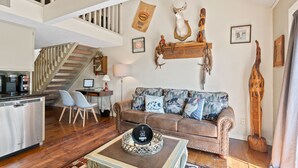 A spacious living area with a staircase, a sofa with patterned cushions, a coffee table with decorative items, and wall-mounted animal trophies. - 2 bed 2 bath Rustic roost loft condo; deck 2 pools; Lake Taneycomo, & amenities  (Branson)