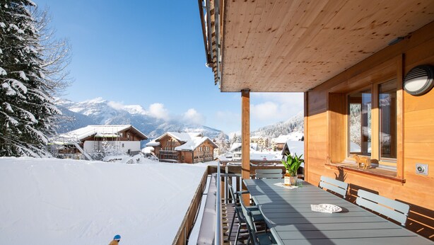A wooden chalet with a balcony overlooking a snowy mountain landscape.