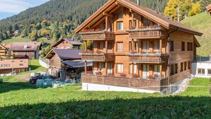 A multi-story wooden chalet with balconies, surrounded by a mountainous landscape.