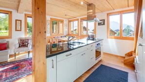 A modern kitchen with wooden beams, large windows, and a view of the outdoors.