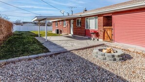 Una casa de ladrillo de un piso con fachada roja, un porche cubierto y una chimenea en el jardín.