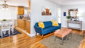 Una sala de estar moderna con un sofá azul, piso de madera y una cocina visible al fondo.