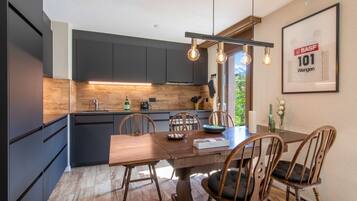 Une cuisine moderne avec des meubles de couleur sombre, une table à manger en bois et un luminaire suspendu.