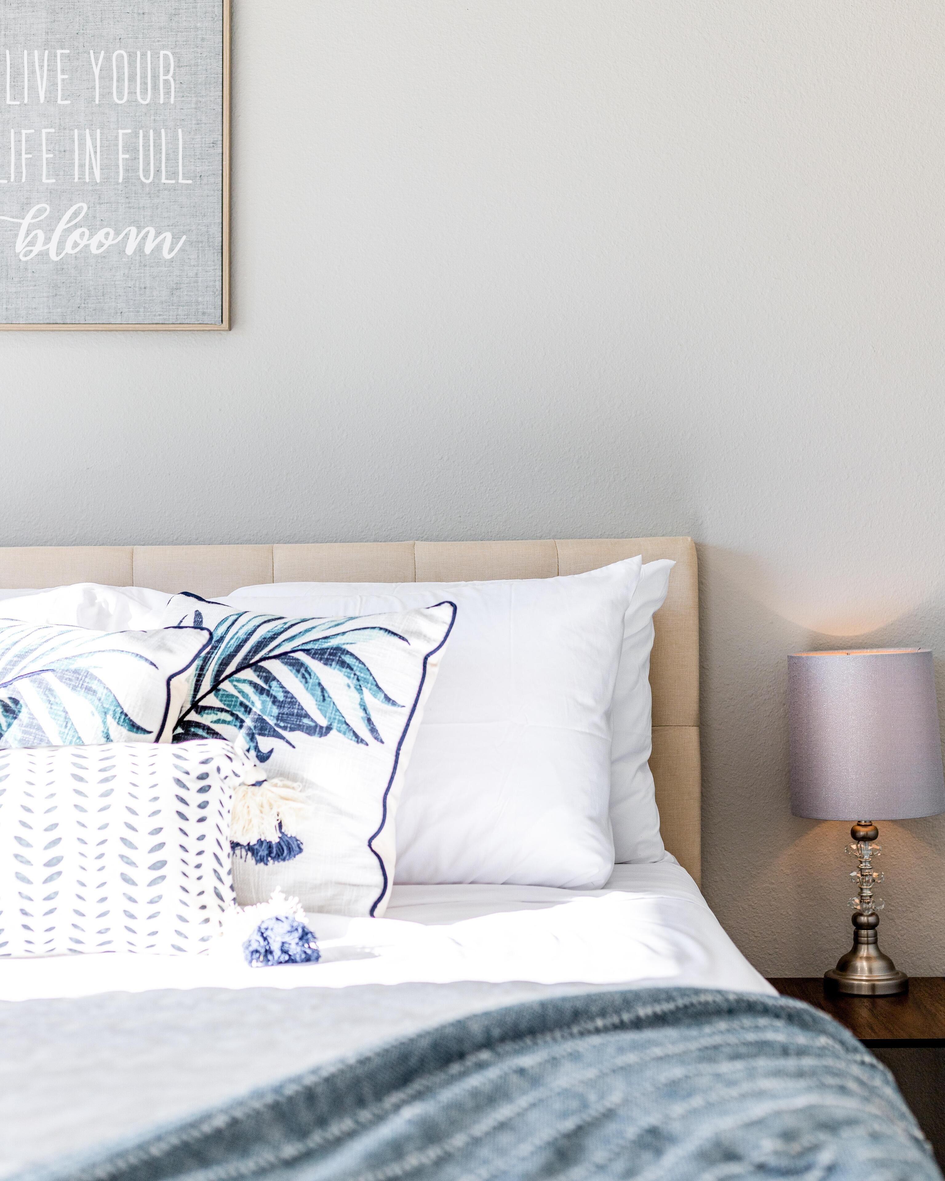 A neatly made bed with a white and blue patterned pillow, a blue and white striped blanket, and a wall-mounted lamp.