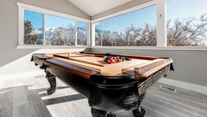 A pool table with a view of mountains through large windows.