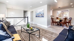 A modern living room with a dark sofa, a glass coffee table, and a dining area with wooden chairs and a table.
