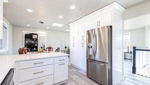A modern kitchen with white cabinetry, a stainless steel refrigerator, and a wooden dining area.