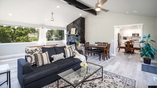 A modern living room with a dark sofa, glass coffee table, and a dining area with wooden furniture.