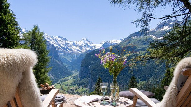 A wooden table with a book and two glasses, set against a mountainous backdrop.