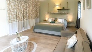 Een slaapkamer met een bed, een bank, een klein rond tafeltje en een raam met gordijnen.