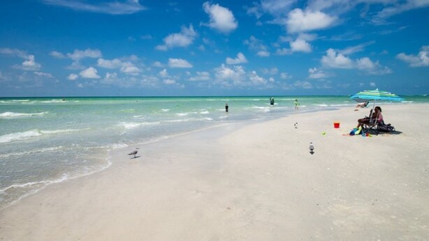 A beach with clear skies, calm waters, and a few people and umbrellas. - Lido Beach House
 (Sarasota)
