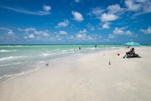 A beach with clear skies, calm waters, and a few people and umbrellas.
