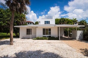 A modern two-story house with a covered patio, a gravel driveway, and a palm tree.