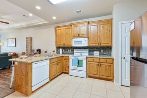 A modern kitchen with wooden cabinets, a built-in microwave, a stainless steel refrigerator, and a central island with a dishwasher.
