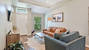 A living room with a brown leather sofa, a gray armchair, a coffee table, and a large window with blinds.