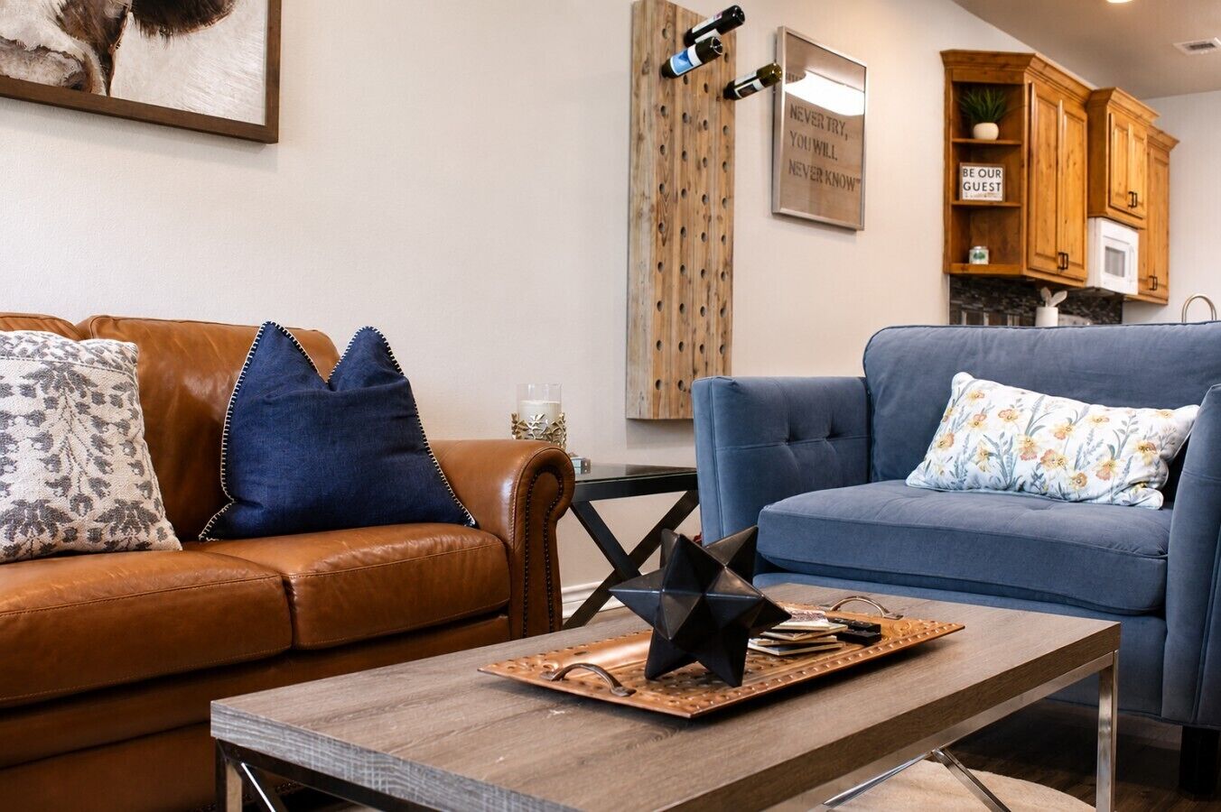Un salon comprenant un canapé en cuir marron, un canapé bleu, une table basse en bois et un coin cuisine avec des meubles en bois et un four à micro-ondes.