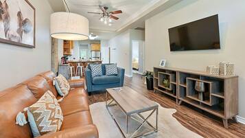 A spacious living room with a leather sofa, a coffee table, and a TV mounted on the wall.