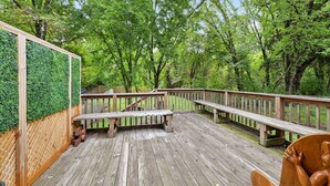 A wooden deck with benches and a wooden railing, surrounded by lush green trees.