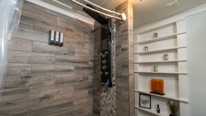 Een moderne badkamer met een douchegedeelte, houten wandtegels, een inbouwplankje met decoratieve objecten en een plafondlamp.