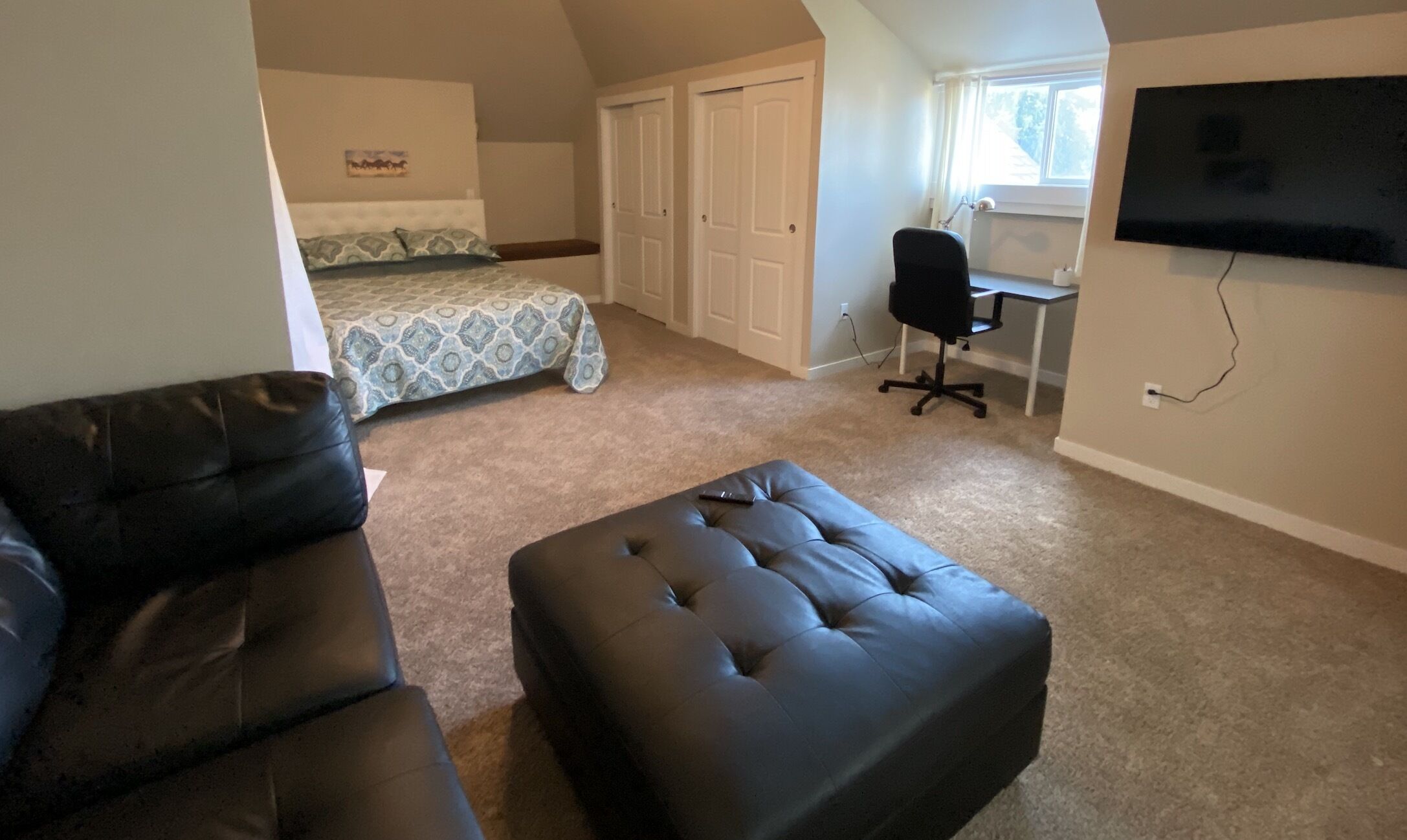 A bedroom with a bed, a desk, a chair, and a TV.