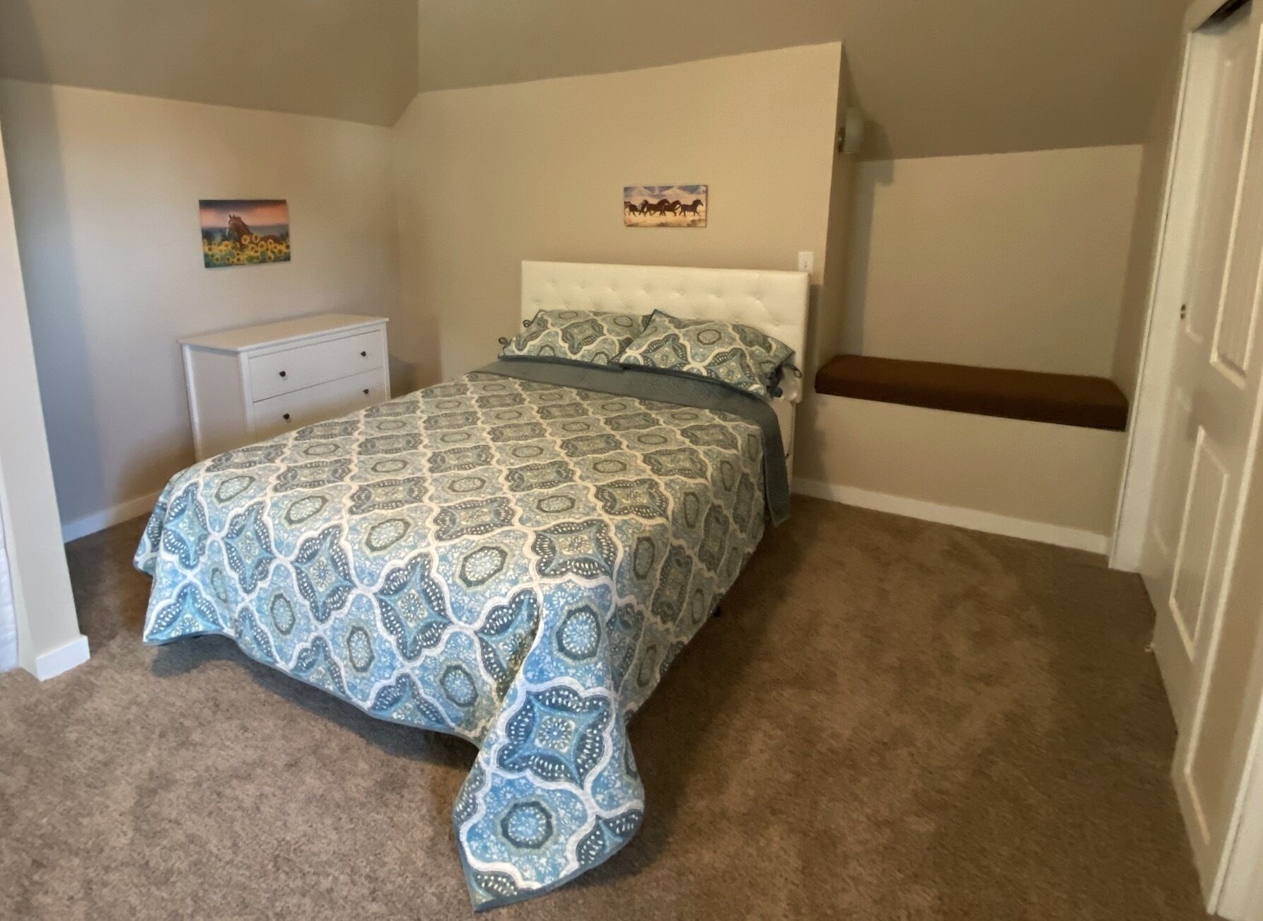 A bedroom with a bed, a nightstand, a bench, and two wall art pieces.