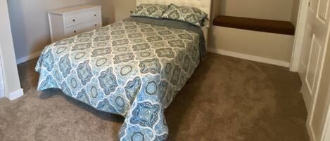 A bedroom with a bed, a nightstand, a bench, and two wall art pieces.