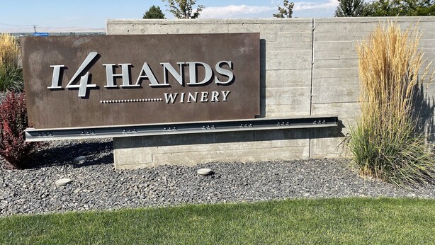 Cartell de I4 Hands Winery amb un fons de fusta i terra de grava al davant.