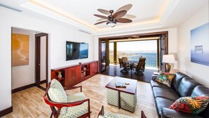 A spacious living area with a ceiling fan, a TV, a dining table with chairs, a sofa with cushions, and a large window offering a view. - 360 Splendor 207A- 2 BR Condo, Breakfast Included (360 Splendor)