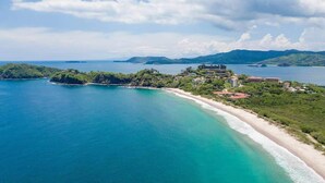 An aerial view of a coastal area with a beach, a large building complex, and surrounding greenery. - 360 Splendor 202-Condo with Breakfast Included (360 Splendor)